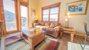 A cozy living room with a leather sofa, wooden coffee table, and a large window with blinds. - Antlers Gulch 502 (Keystone)