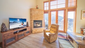 A living room with a stone fireplace, wooden entertainment unit, and large windows. - Antlers Gulch 502 (Keystone)