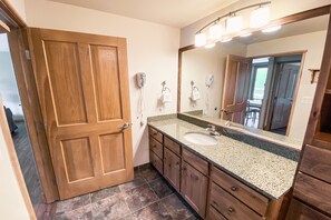 A bathroom with a wooden door, a sink, a mirror, and a hairdryer. - Black Bear 8055 (Keystone)