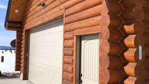 Une cabane en rondins avec une porte de garage, une porte en bois et un thermomètre en métal fixé au mur.