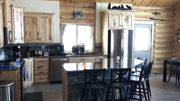 Une cuisine spacieuse avec des meubles en bois, un îlot central doté de tabourets de bar, un réfrigérateur en acier inoxydable et un luminaire suspendu.