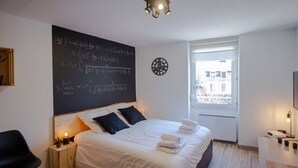 A modern bedroom with a large bed, a blackboard with mathematical equations, a clock, and a window with a city view. - THE SQUARE ROOT (Dijon)
