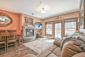 A cozy living room with a fireplace, wooden furniture, and large windows.