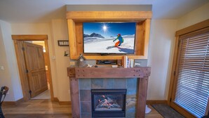 Una sala de estar con chimenea, un televisor montado encima y una puerta que da a otra habitación.