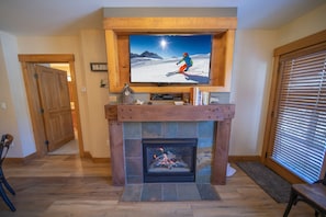 A living room with a fireplace, a television mounted above it, and a door leading to another room. - Springs 8859 (Keystone)