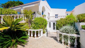 A white building with a tiled roof, a paved courtyard, and various plants. - Montenegro Superbly Located Family Vila With Game Room & Pool (Carvoeiro)