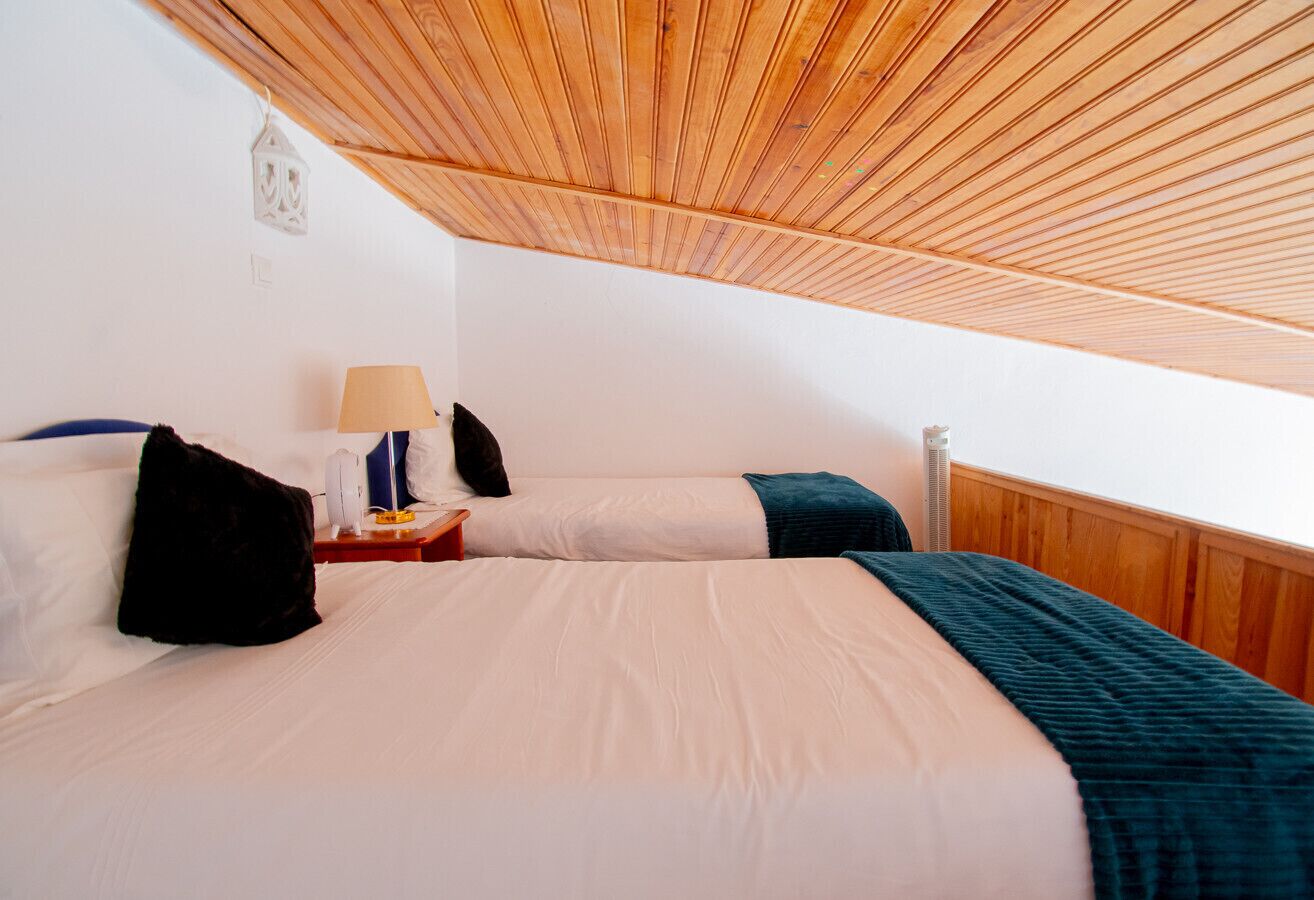 Quarto com duas camas, mesa de cabeceira com abajur e teto de madeira.