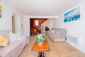 Una sala de estar con dos sofás, una mesa de centro con un centro de mesa floral y un cuadro de barcos en la pared.