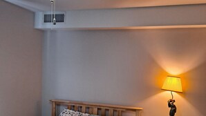 Quarto com cama, mesa de cabeceira com abajur, ventilador de teto e saída de ar na parede.