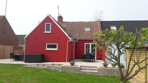 Une maison rouge avec un toit en tuiles, un petit porche avec des meubles d’extérieur et un chemin en briques menant à l’entrée.
