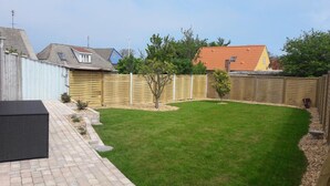 Un jardin avec une terrasse dallée, une pelouse et une clôture en bois.