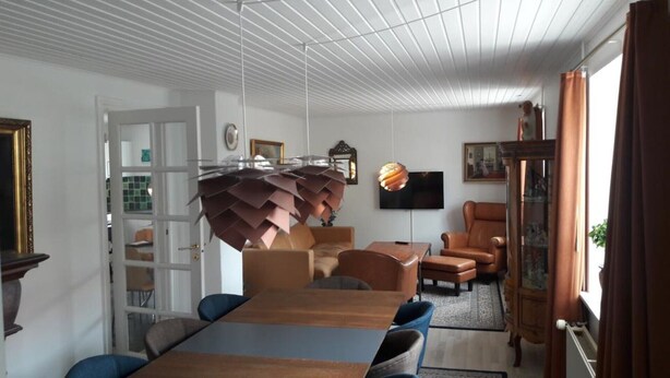 Un salon moderne avec une table à manger en bois, des canapés en cuir et une œuvre d’art originale en papier suspendue au plafond.