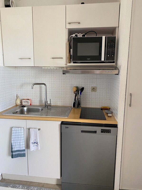 A compact kitchen with white cabinets, a built-in microwave, a sink, and a dishwasher. - Apartment at the cliffs (Agde)