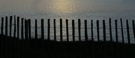 Un coucher de soleil sur une mer calme, avec une clôture en bois au premier plan.