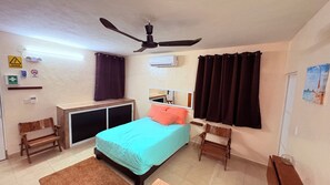 A bedroom with a bed, a ceiling fan, a window with curtains, a bedside table, a mirror, and a wall-mounted air conditioner. - Vacation Home (Isla Mujeres)