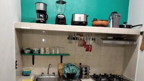 A compact kitchen with a gas stove, a sink, and various appliances like a coffee maker and a blender. - Vacation home (Isla Mujeres)