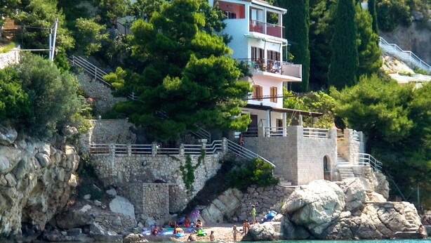 A coastal building with a stone staircase leading to a balcony, surrounded by greenery and overlooking a body of water. - Beach House Villa Antares, Penthouse apt. A1 (Pisak)