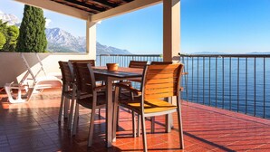 A covered outdoor dining area with a table and chairs, overlooking a body of water and mountains. - Beach House Villa Antares, Penthouse apt. A1 (Pisak)