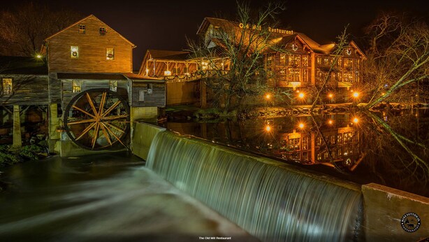 Historiallinen mylly, jossa on vesiratas, puisia rakennuksia ja joen varrella sijaitseva ravintola nimeltä ”The Old Mill Restaurant”, joka on erityisen kaunis yöllä.