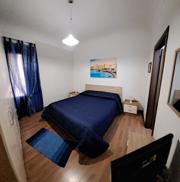 A bedroom with a bed, bedside tables, a nightstand, a painting, and a window with curtains.