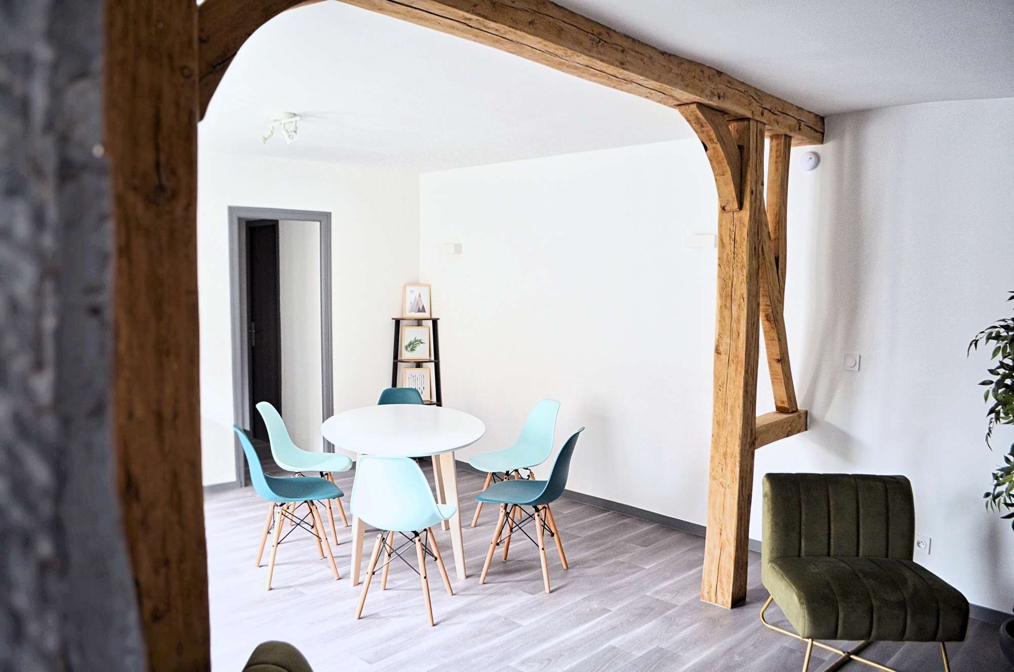A dining area with a round table and four chairs, a wooden beam structure, and a green armchair.