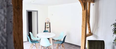 A dining area with a round table and four chairs, a wooden beam structure, and a green armchair.