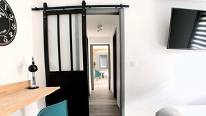 Ein modernes Zimmer mit Schreibtisch, Stuhl, Bett und einem an der Wand befestigten Fernseher.