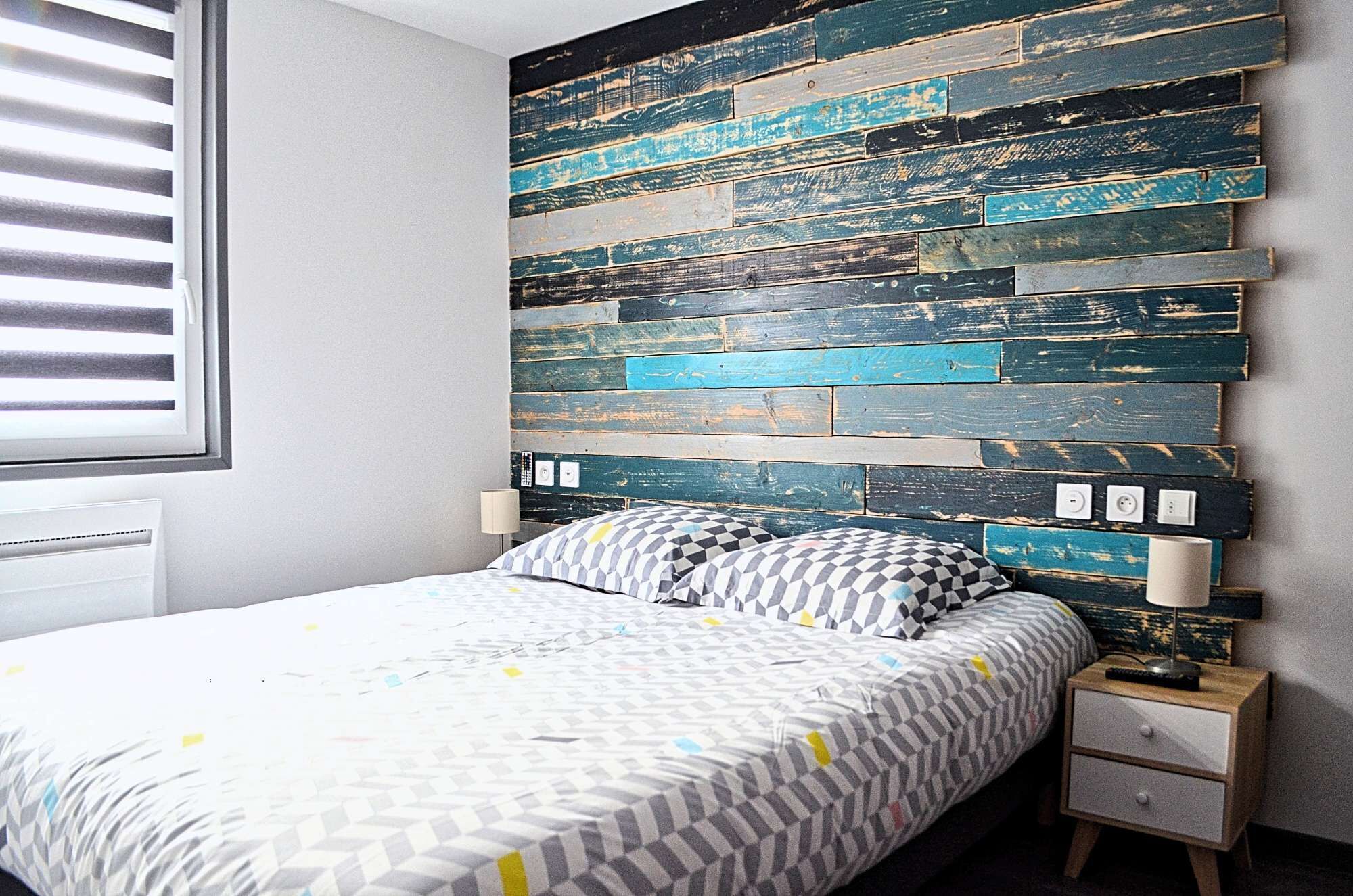Een slaapkamer met een bed, nachtkastje, een wandlamp en een raam met zonwering.