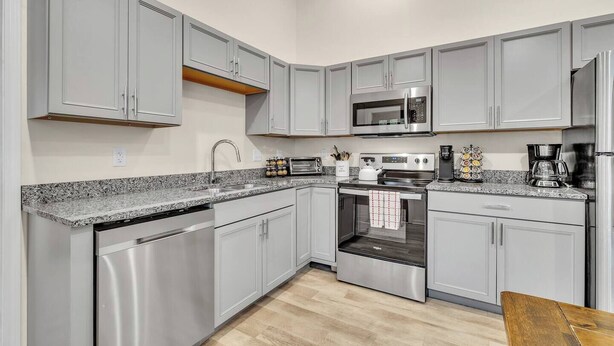 A modern kitchen with grey cabinets, stainless steel appliances, a granite countertop, and a wooden dining table. - Walk Downtown | Parkside | City View | Beautifully Remodeled (Ann Arbor)