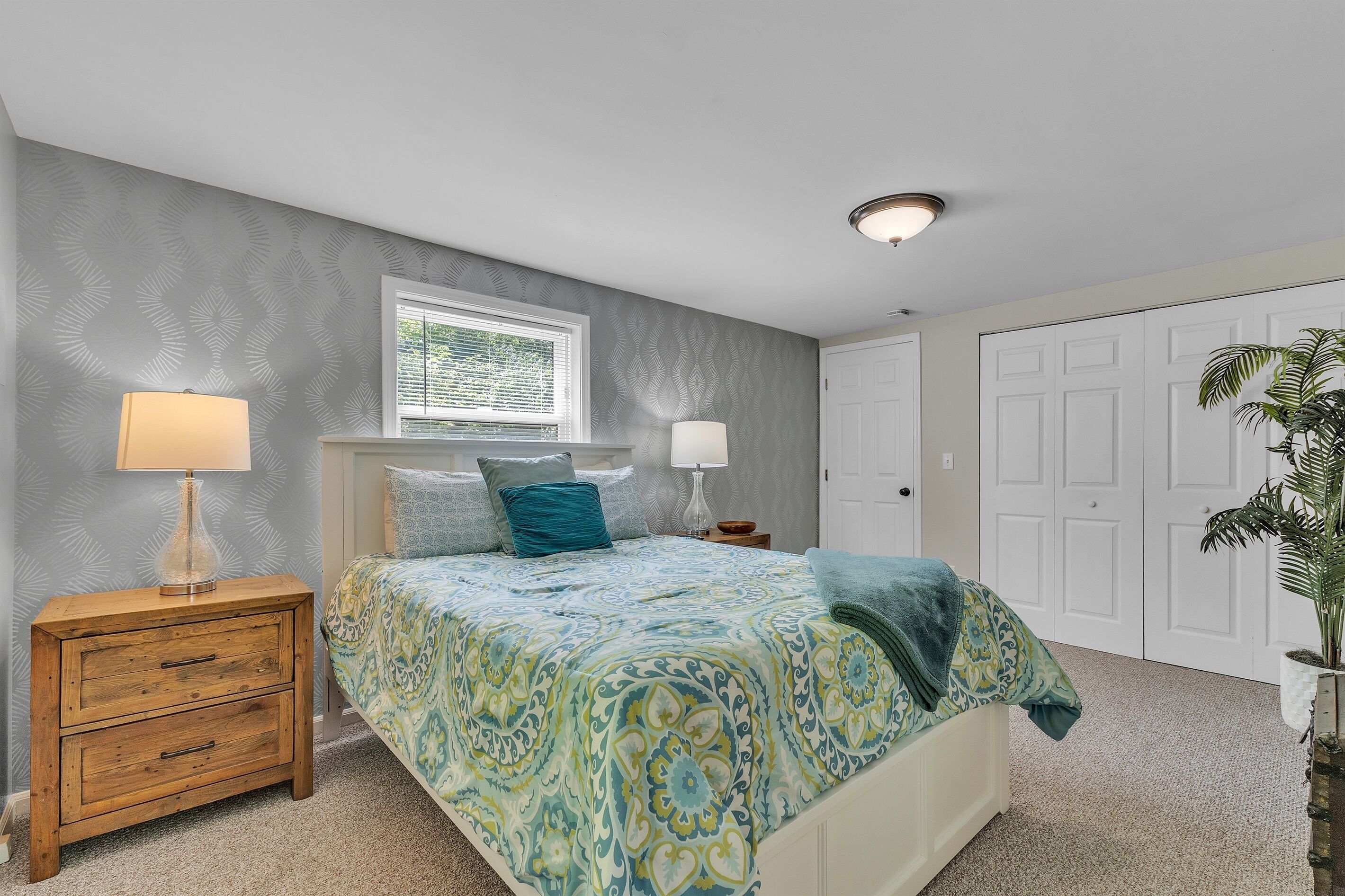 A bedroom with a bed, two bedside tables, a window, and a door.