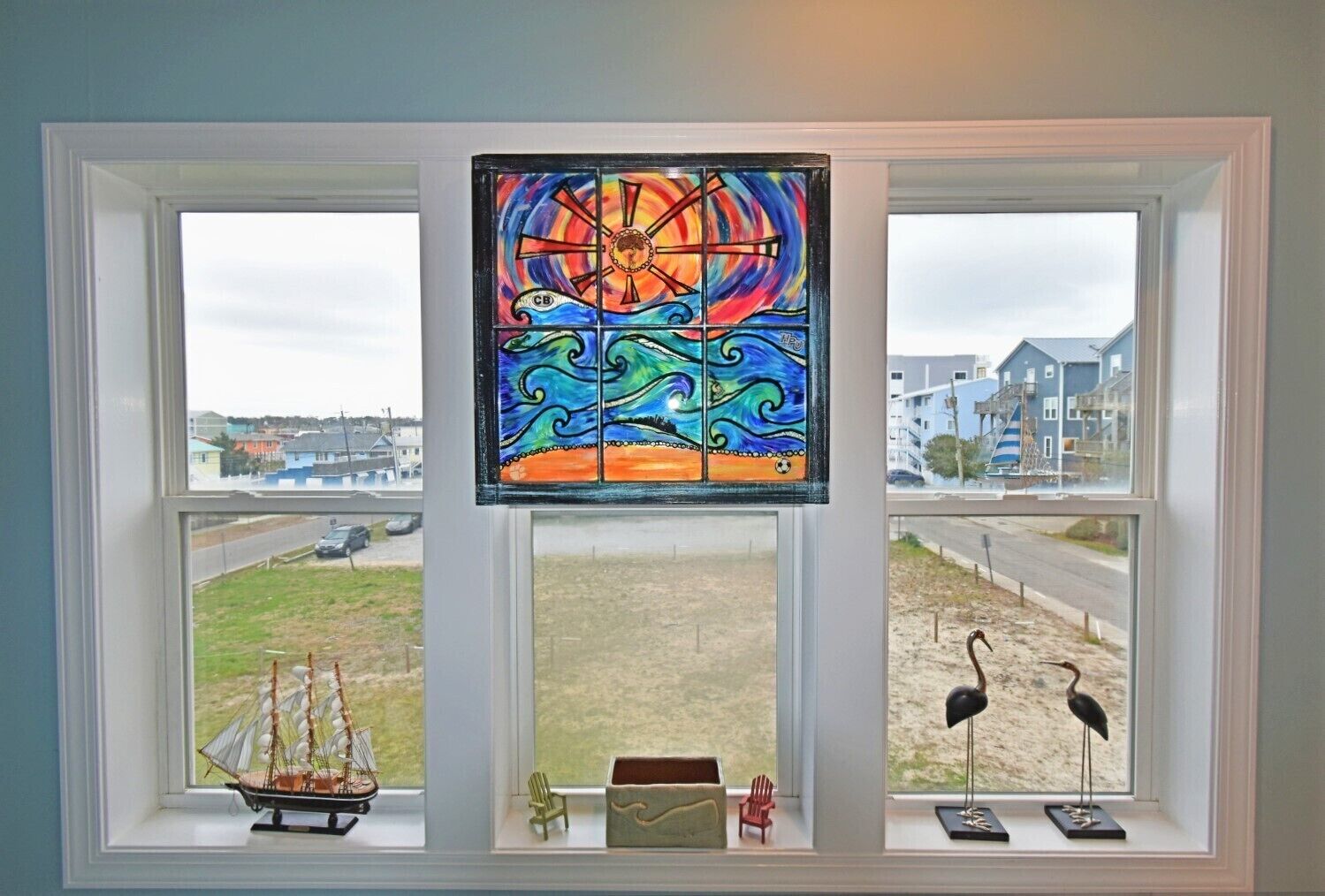 A stained glass window with a ship model, two chairs, and two bird figurines on a window sill.