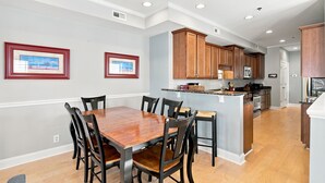 A modern kitchen with wooden cabinets, a central island, and a dining area with a wooden table and chairs. - Blue Heaven - Walk to Beach & Boardwalk, Ocean and Sunset Views, Dog-Friendly (Carolina Beach)