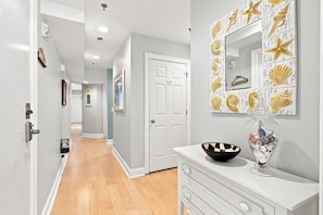 A hallway with a white door labeled 'OWNERS CLOSET,' a white console table with a black bowl and decorative glass vase, and a wall with a seashell and starfish pattern.