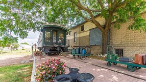 A historic building with a green tower, a covered porch, and a brick wall. There are vintage suitcases and a cart with pots on the sidewalk.