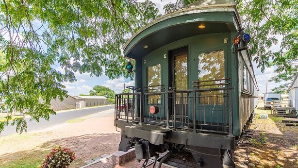 A green train car with a small porch and a potted plant in front.