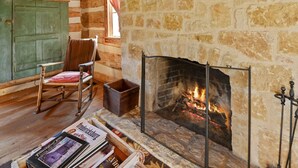 L’intérieur d’un chalet confortable, avec des murs en rondins de bois, une cheminée en pierre, des meubles en bois et une fenêtre agrémentée de rideaux.
