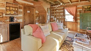 L’intérieur chaleureux d’un chalet avec un canapé, des murs en bois, un escalier et un coin cuisine.