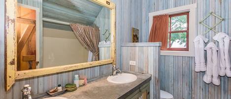 A bathroom with wooden walls, a large mirror, two sinks, a toilet, and towels hanging on hooks.
