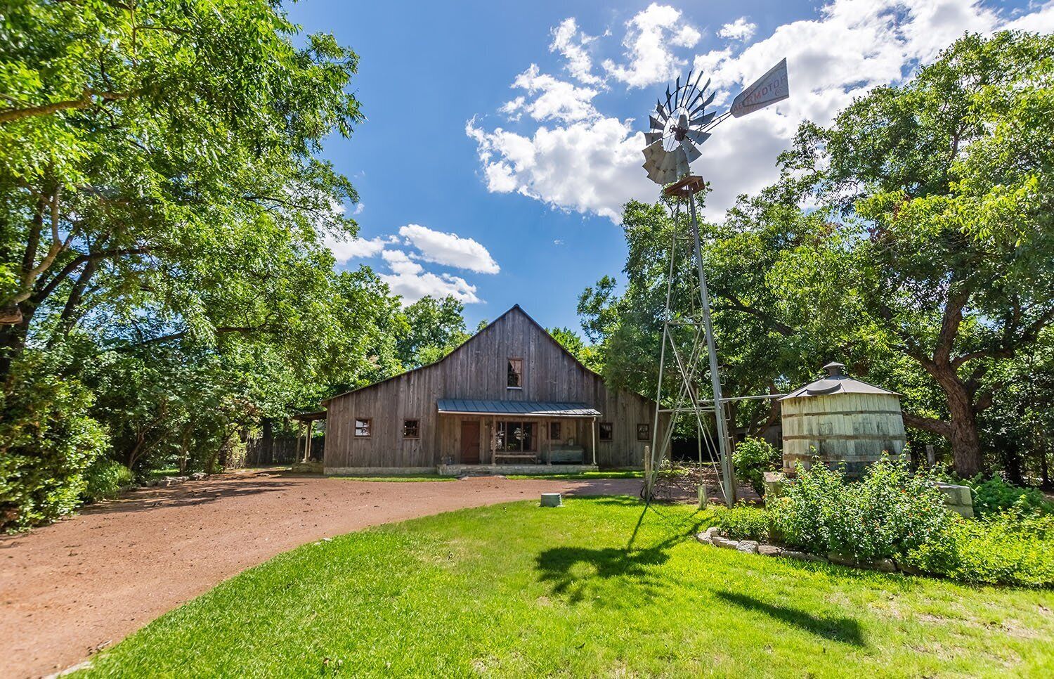 A rustic barn with a porch, surrounded by lush greenery and a clear sky.
