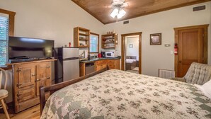 A bedroom with a bed, wooden cabinets, a television, a microwave, and a kitchenette.