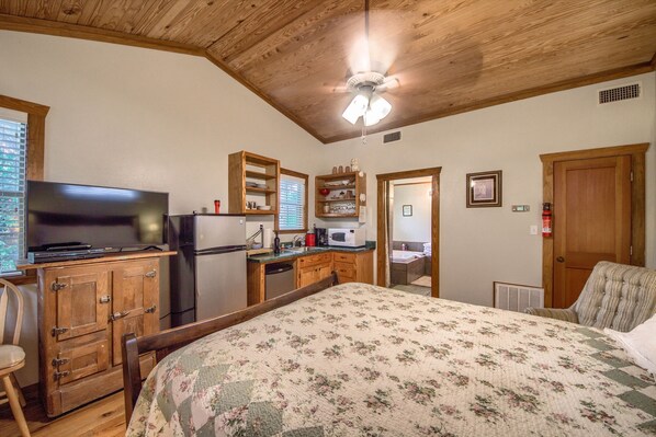 Un dormitorio con cama, armarios de madera, televisión, microondas y kitchenette.