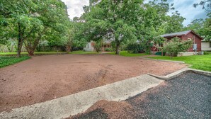A spacious outdoor area with a gravel path, surrounded by mature trees and a red building.