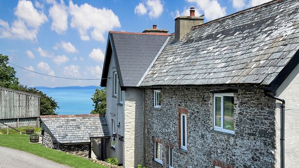 Un bâtiment en pierre avec un toit en pente, un petit porche et une vue sur la mer.