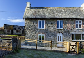 A stone building with a wooden fence, a gravel driveway, and a clear blue sky.