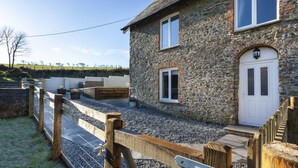 Une maison en pierre avec une porte blanche, un petit porche et une clôture en bois.