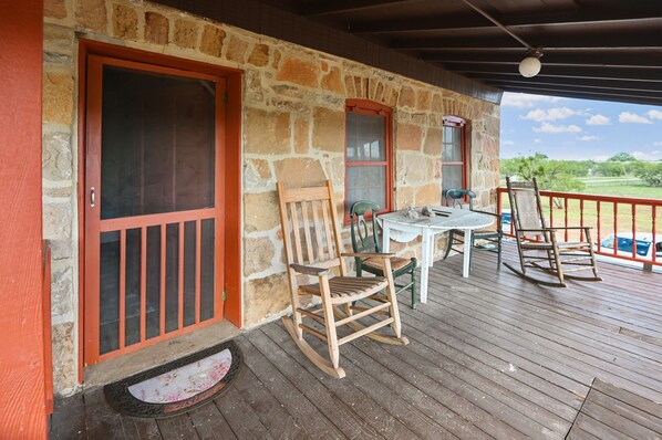 A wooden deck with a stone wall, a wooden rocking chair, a table, and a chair.