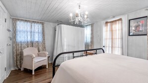 A bedroom with a bed, a chair, a chandelier, and curtains. - Charming Private 2-Story Cottage - Romantic Getaway - Close to Downtown (Fredericksburg)