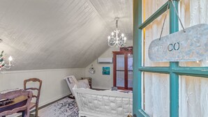 A cozy attic bedroom with a sloped ceiling, a white bed, a wooden chair, a chandelier, and a 'WELCOME' sign. - Charming Private 2-Story Cottage - Romantic Getaway - Close to Downtown (Fredericksburg)