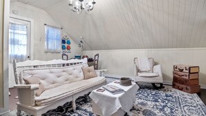 A cozy room with a white sofa, a small table with a book, a chair, and a collection of suitcases. - Charming Private 2-Story Cottage - Romantic Getaway - Close to Downtown (Fredericksburg)