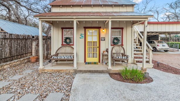 A small, single-story building with a porch, two wicker chairs, a yellow door, and a sign indicating furnished rooms. - Charming Private 2-Story Cottage - Romantic Getaway - Close to Downtown (Fredericksburg)
